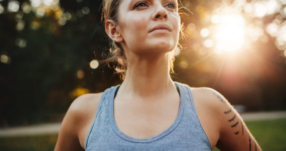 Close up portrait of fit young woman in sportswear standing outdoors and looking away. Confident fitness model in park.