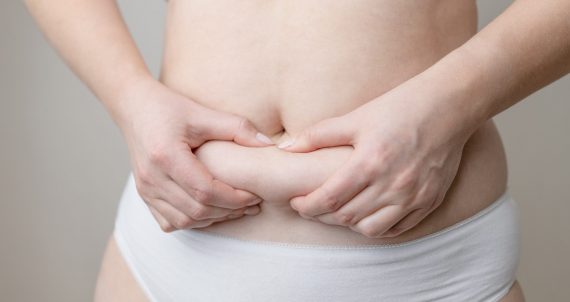 Closeup cropped of unrecognizable fat woman hand holding fat belly on white background.