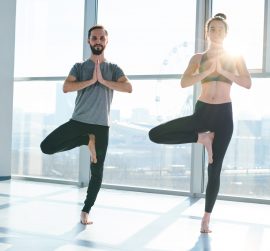 Young active couple keeping balance while standing on one leg with their hands put together by chest
