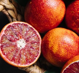Whole and sliced blood oranges in a basket on blue table background. Close up.